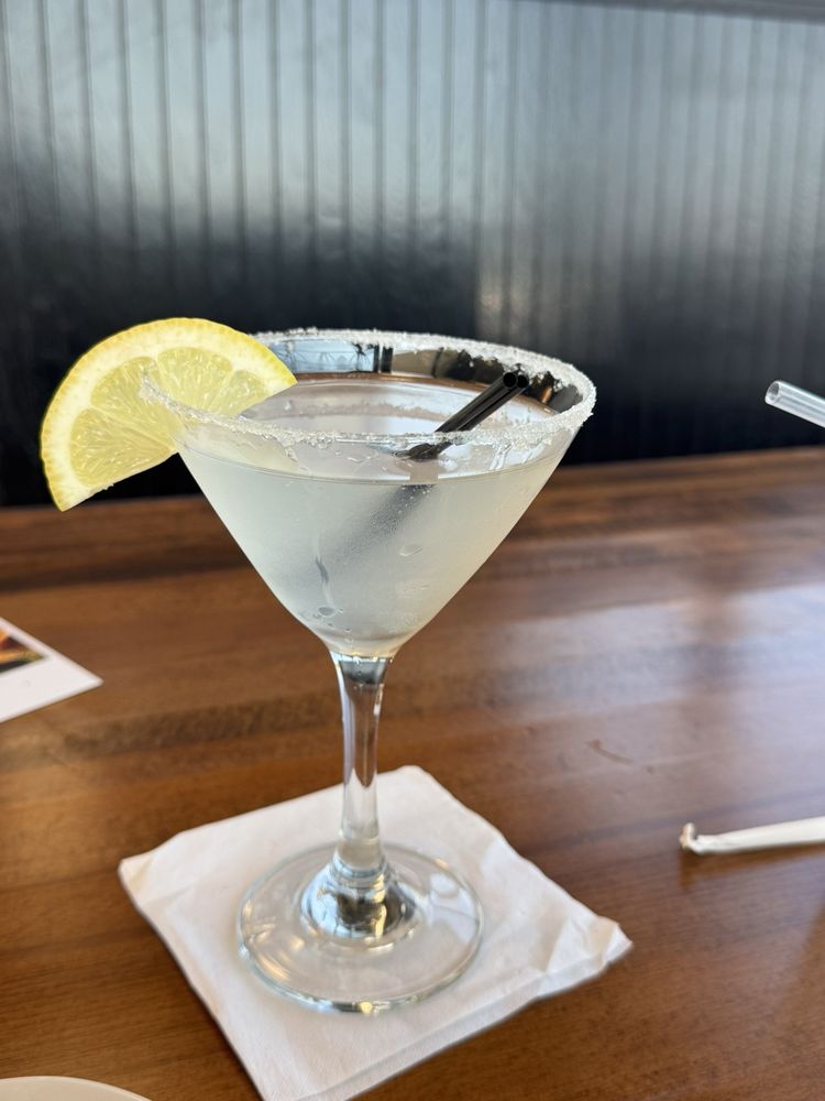 A sugar-rimmed lemon drop martini with a lemon wheel, on the bar top