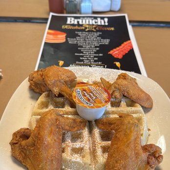 Fried chicken wings served over a waffle with a cup of syrup, beside the brunch menu